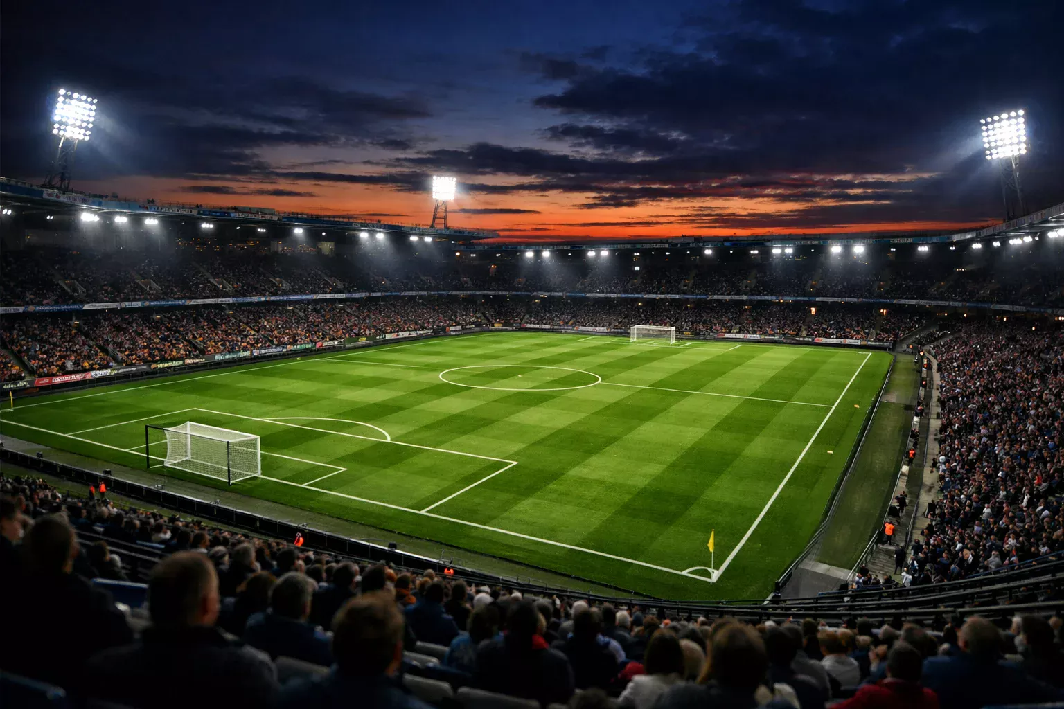 Stade de football éclairé en soirée vu depuis les tribunes avec le terrain en gazon naturel